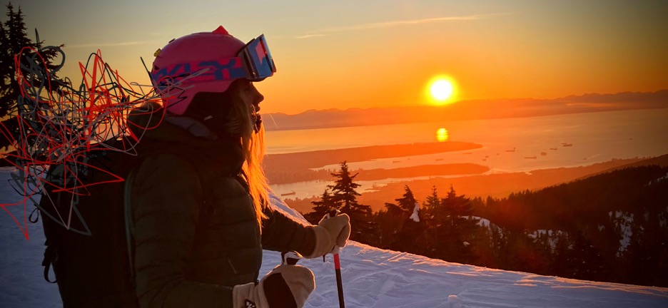 A skier stands on the top of a mountain at sunset. She is looking off into the distance. Chaotic scribbles drift from the back of her head while the stunning view remains unhindered in front of her.